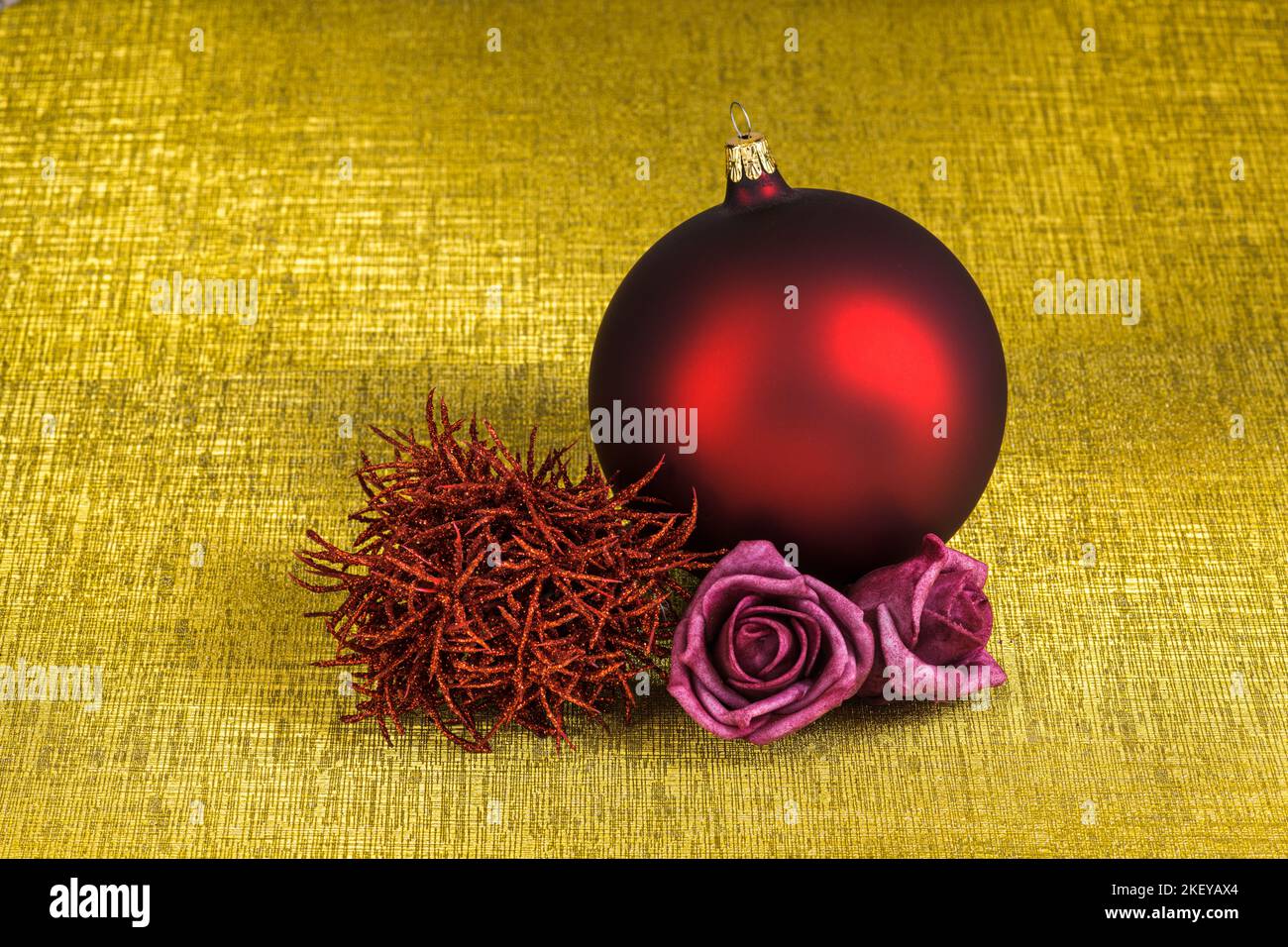 Décocration de Noël avec une boule de noël rouge et deux roses de feutre rose isolées sur un fond doré avec texture. Banque D'Images