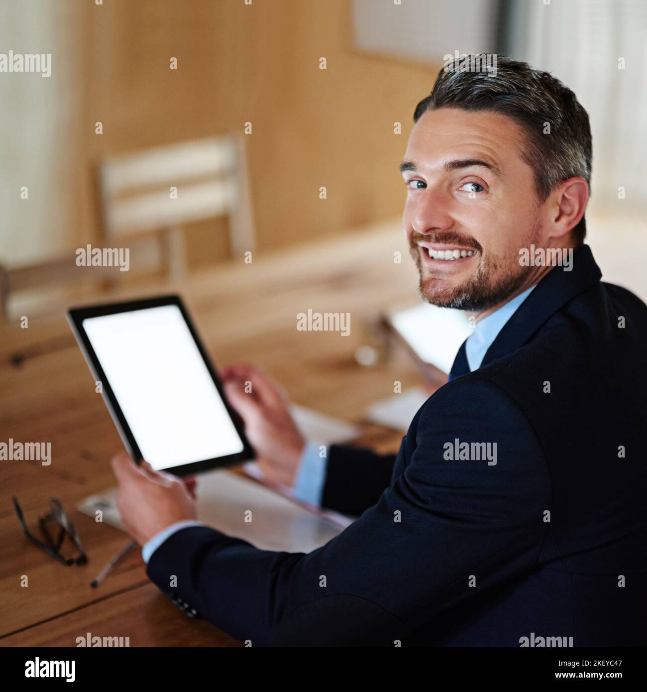 Le site Web parfait pour les professionnels d'affaires. Portrait d'un cadre souriant à l'aide d'une tablette numérique tout en étant assis seul à une table dans un bureau. Banque D'Images