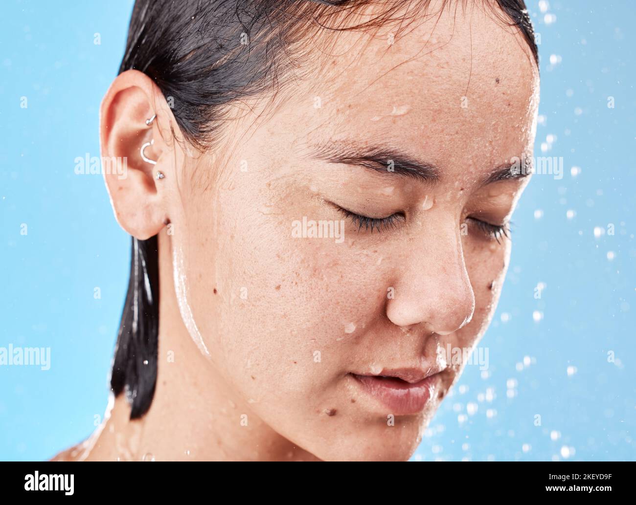 Calme, eau et femme dans la douche pour le toilettage, l'hygiène et se détendre sur un fond bleu studio. Nettoyage, soin de la peau et modèle asiatique relaxant Banque D'Images