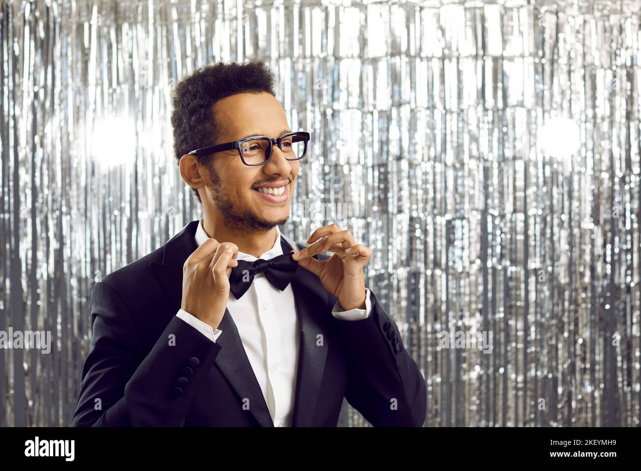 Joyeux jeune homme ethnique en tuxedo et des lunettes stylées qui ajustent son noeud papillon Banque D'Images