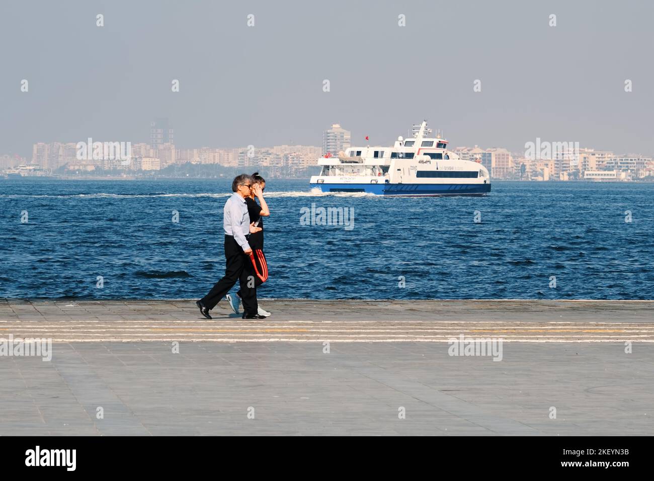 Izmir, Turquie - octobre 2022 : couple marchant au bord de la mer et un ferry à Kordon, Alsancak, Izmir, Turquie. Banque D'Images