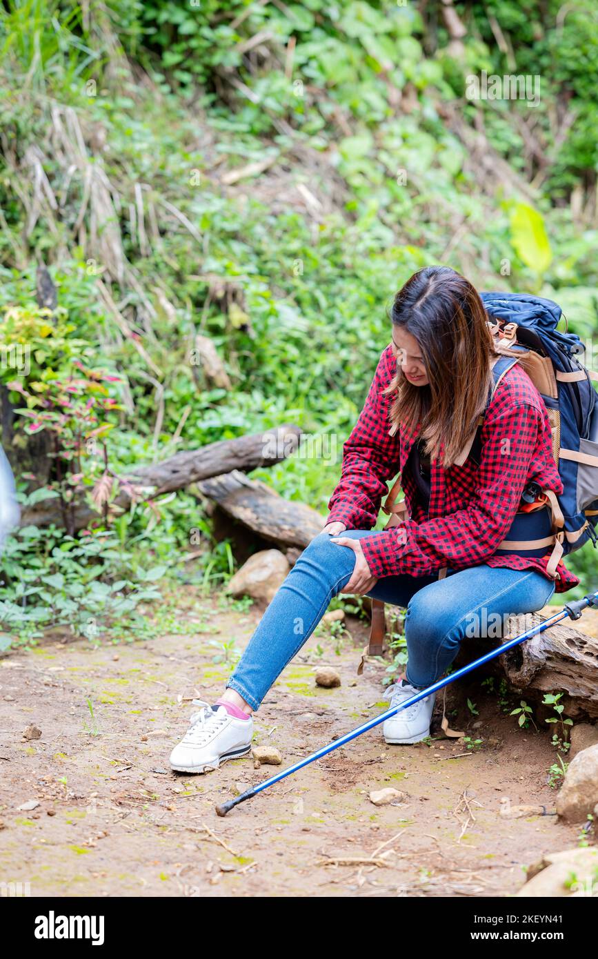 Femme asiatique dans un chapeau et un sac à dos avec un poteau de trekking assis tout en prendre un repos dans la forêt Banque D'Images