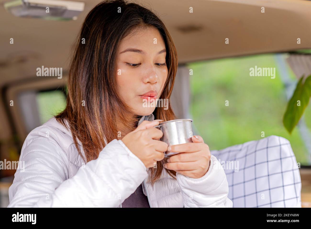 Femme asiatique tenant une boisson chaude à l'intérieur du campervan profitant de l'activité de camp dans la nature Banque D'Images