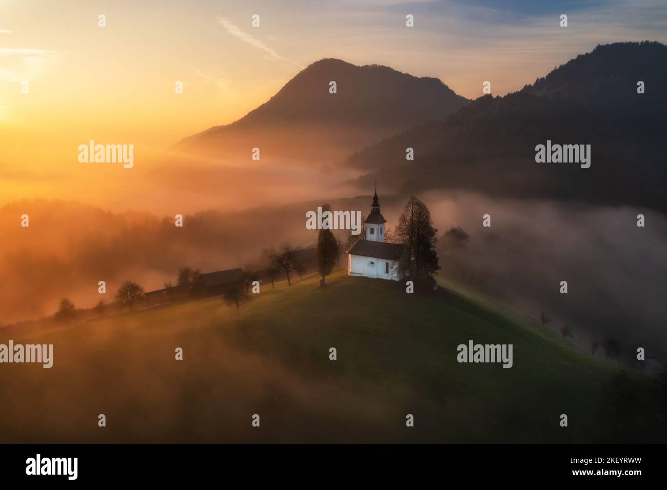 Vue aérienne de drone de petite belle église sur la montagne en Slovénie dans les rayons du soleil à l'aube. Paysage d'automne Banque D'Images