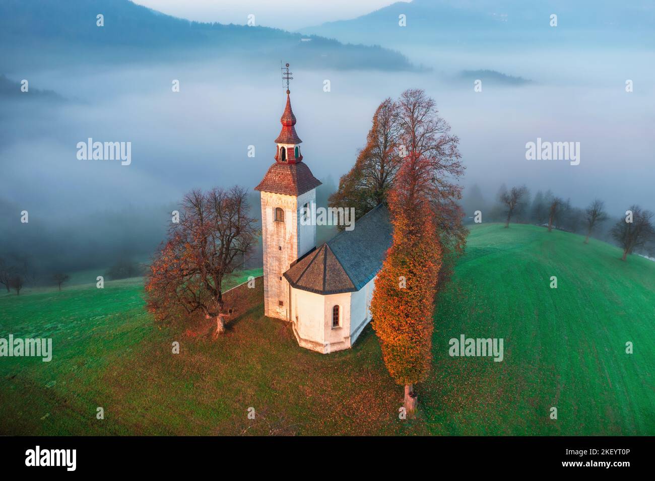 Vue de dessus de la petite belle église sur la montagne en Slovénie à l'aube ou au coucher du soleil. Automne matin paysage prise de drone aérienne Banque D'Images