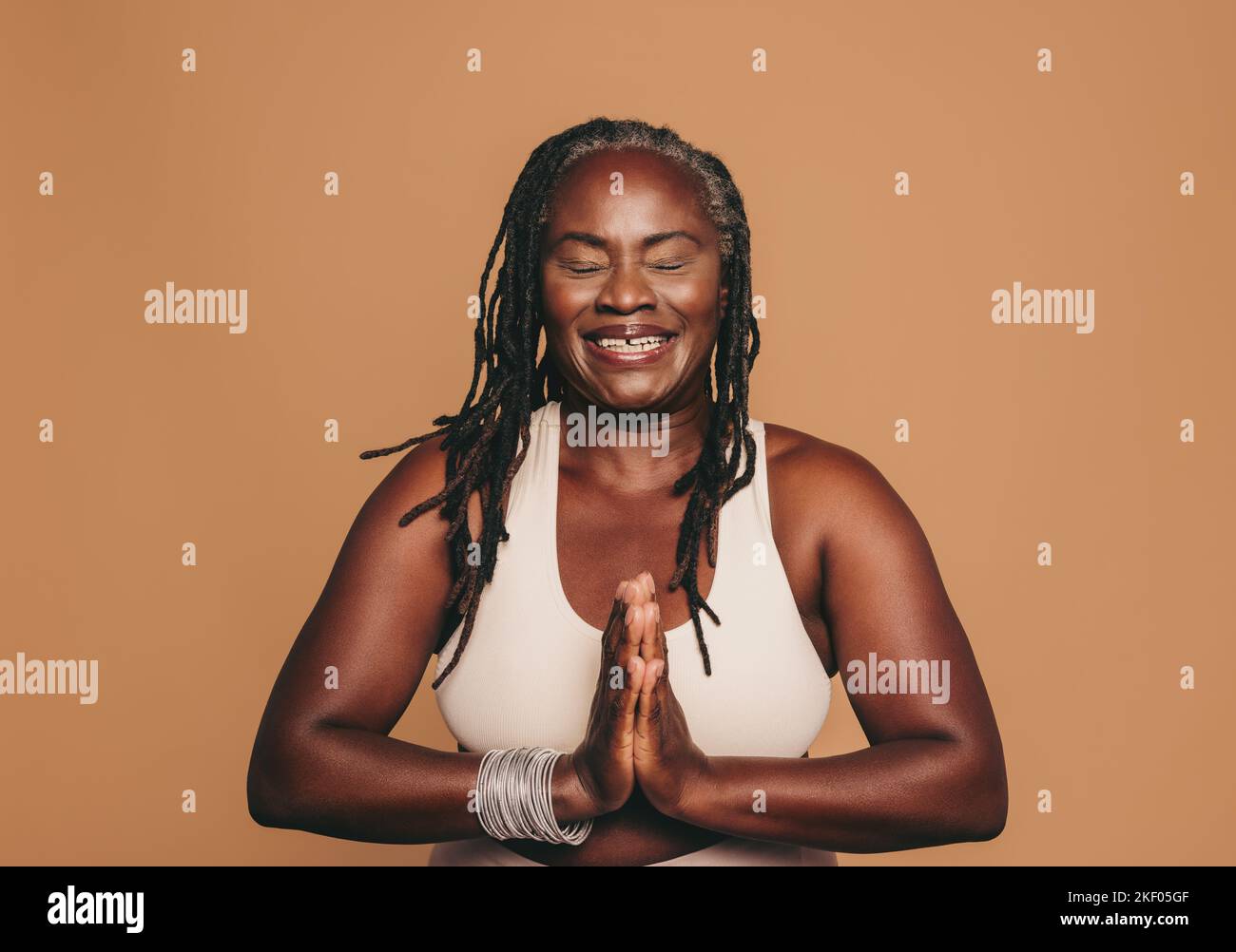 Bonne femme méditant avec ses yeux fermés et ses mains en position de prière. Femme souriante avec des dreadlocks pratiquant le yoga dans un studio. Sport mature Banque D'Images