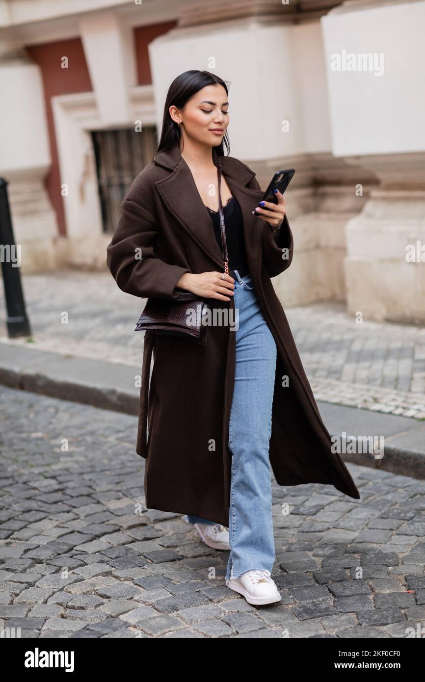 pleine longueur de femme en manteau et jeans marchant à prague et regardant  le smartphone, image de stock Photo Stock - Alamy
