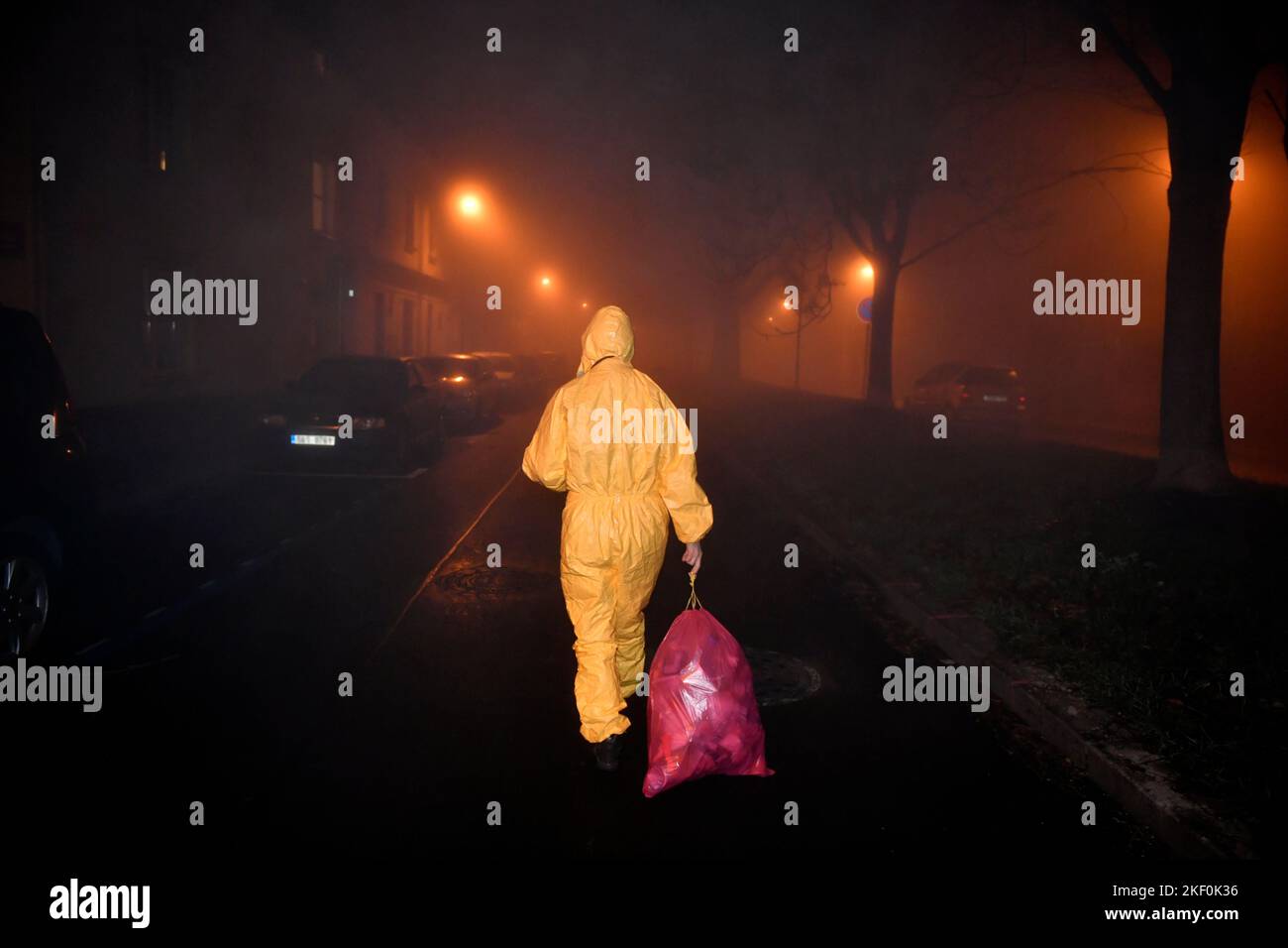 une personne dans le jaune dans l'ensemble marchant sur la route de nuit fumighgy tenant le sac poubelle Banque D'Images