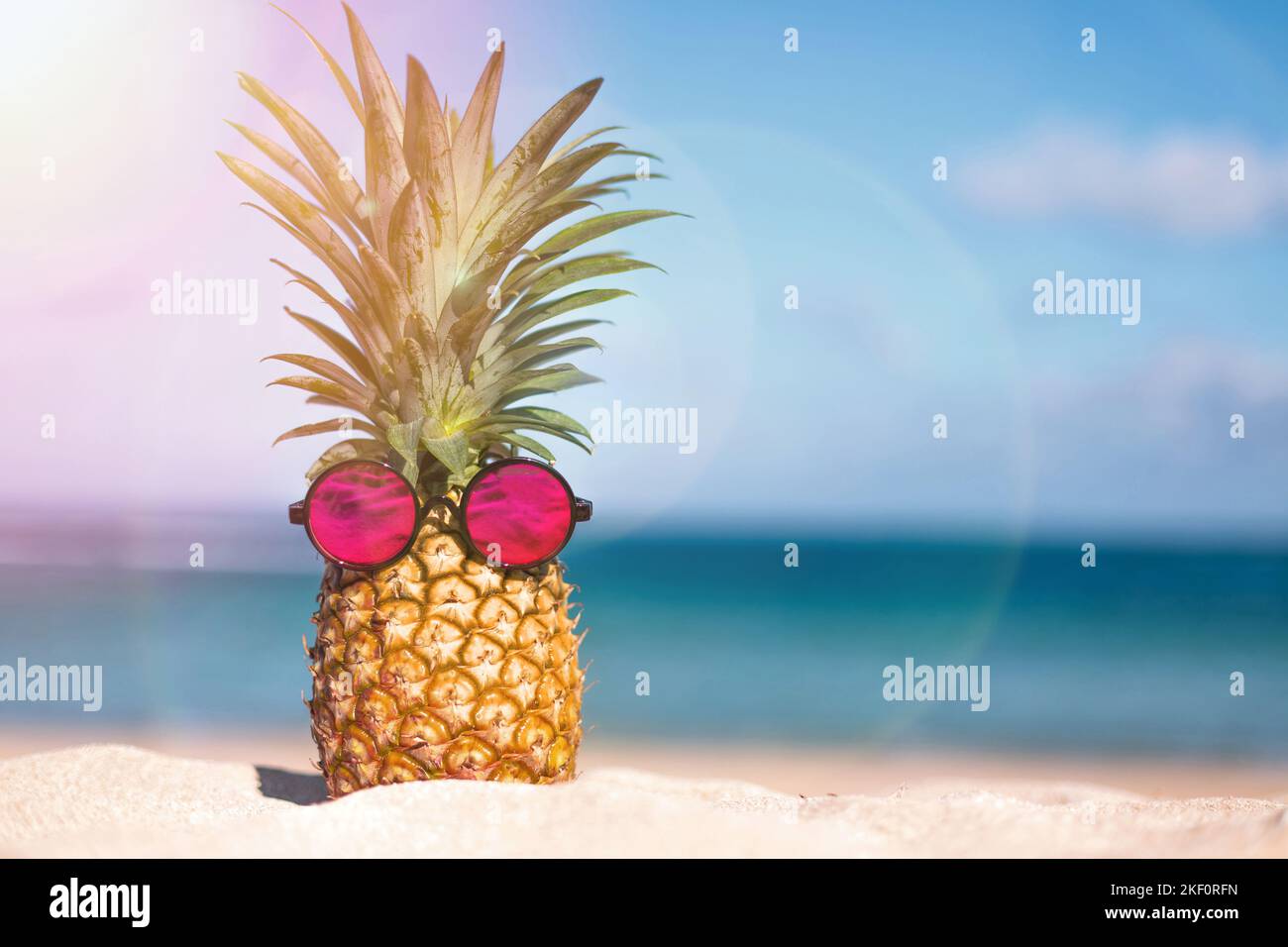 Ananas tropical créatif dans des lunettes de soleil roses sur une plage de sable Banque D'Images