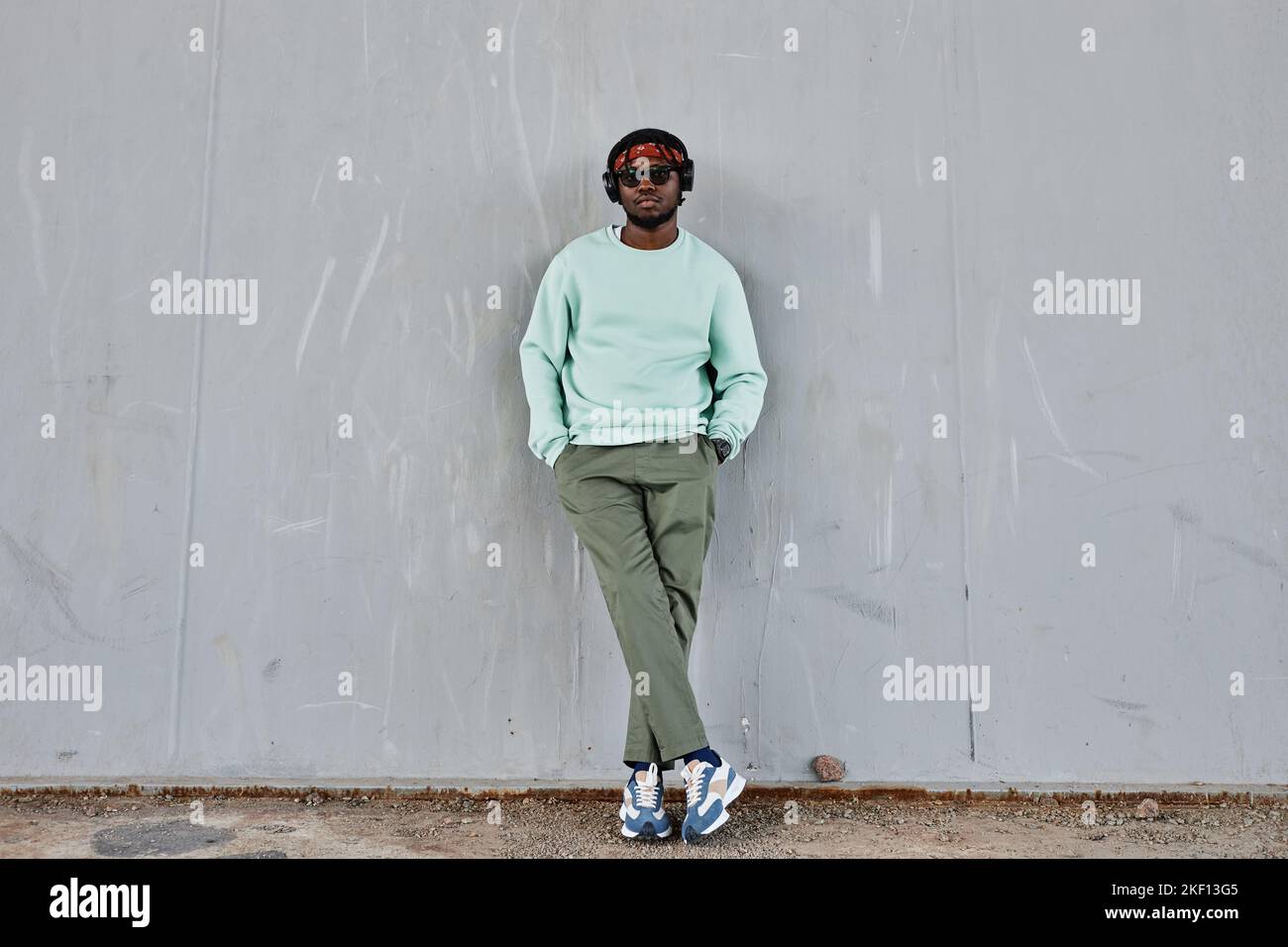 Portrait minimal en longueur d'un jeune homme noir portant des vêtements de style urbain pendus sur un mur de béton à l'extérieur, espace de copie Banque D'Images