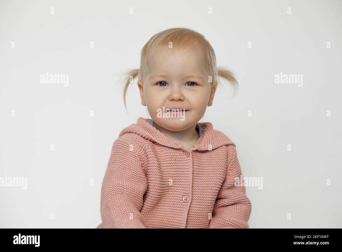 Jolie petite fille souriante isolée sur blanc. Portrait d'un enfant heureux en studio. Enfant blond aux cheveux avec une expression du visage joyeuse en tricot rose Banque D'Images