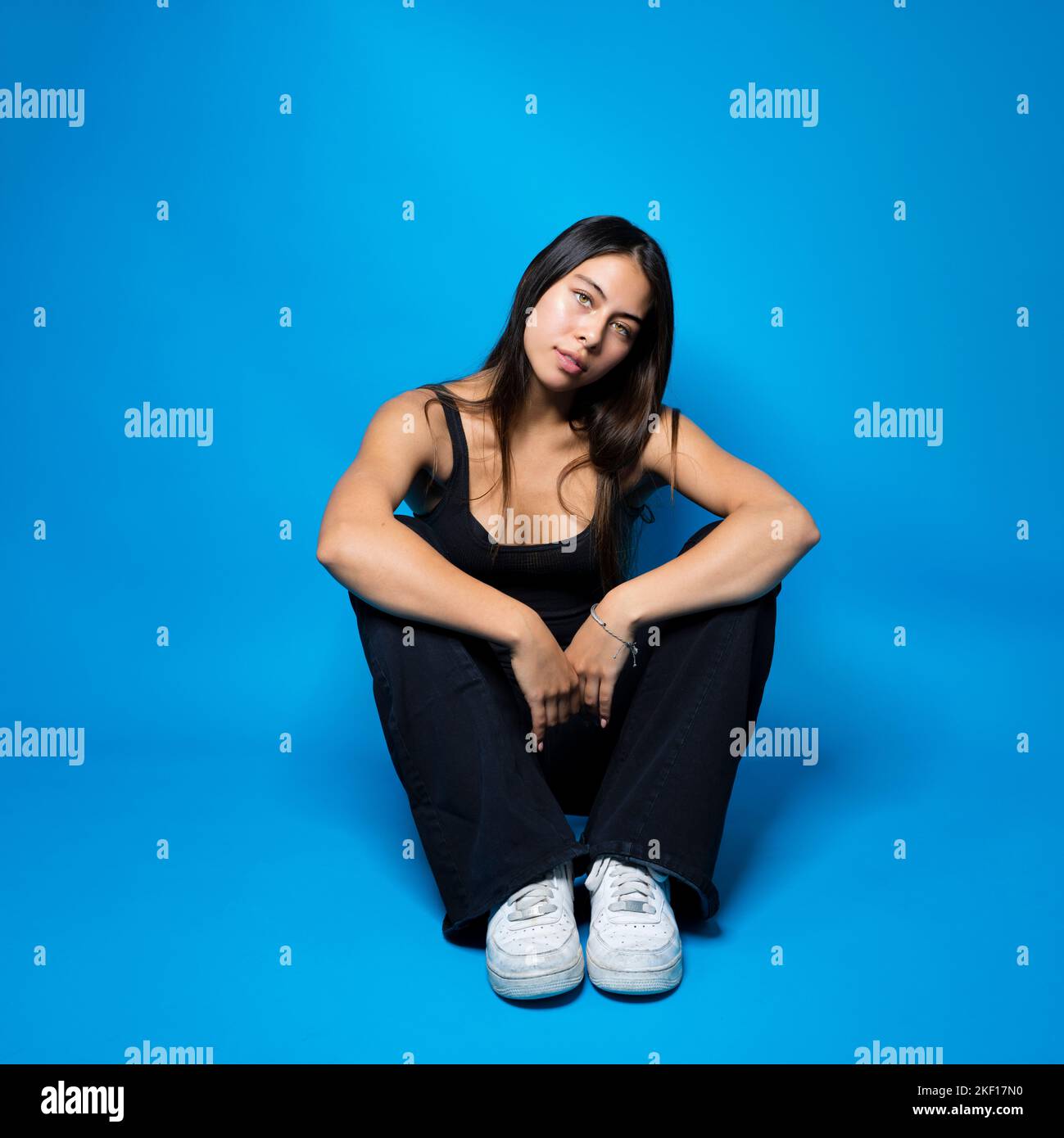 Teen multiracial assis sur le sol en position fœtale sur fond bleu avec espace de copie Banque D'Images