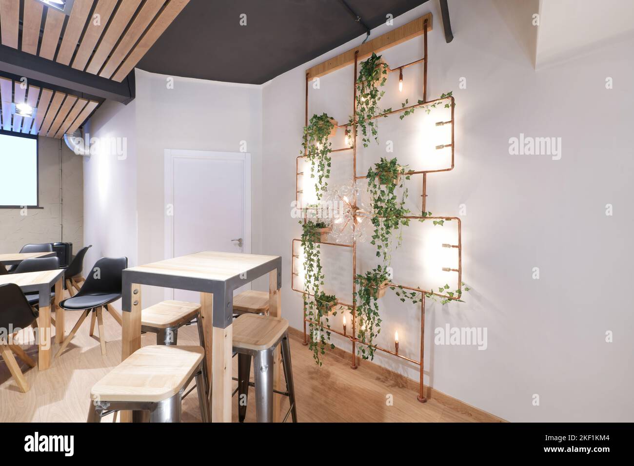 Une salle de restaurant avec de grandes tables et chaises en bois et une étagère en cuivre avec des plantes artificielles et des parquets Banque D'Images
