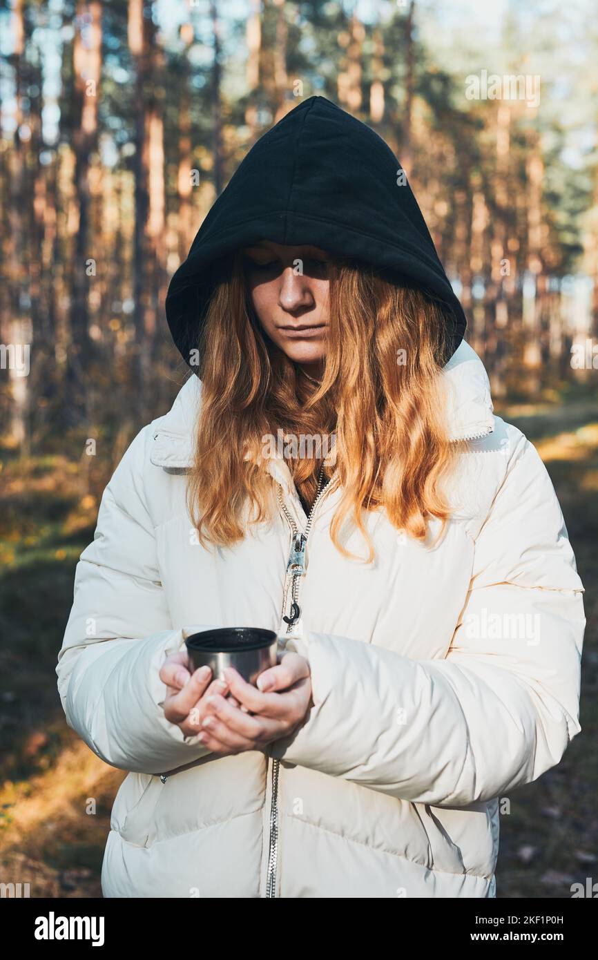 Femme dans une hotte ayant une pause pendant le voyage d'automne tenant une tasse avec une boisson chaude de thermos fiole le jour d'automne froid. Fille active errant dans une forêt ac Banque D'Images