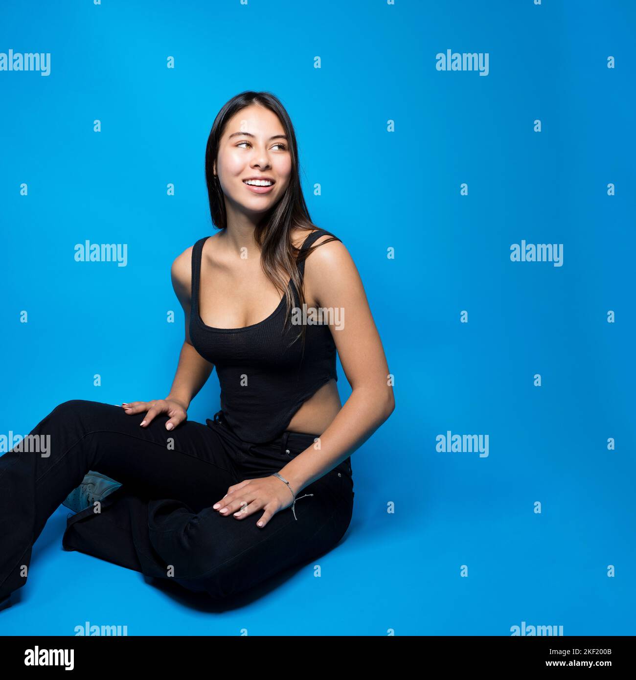 Belle teen multiraciale Femme assise à pieds croisés sur le sol regardant droit Copy Space sur fond bleu isolé Banque D'Images
