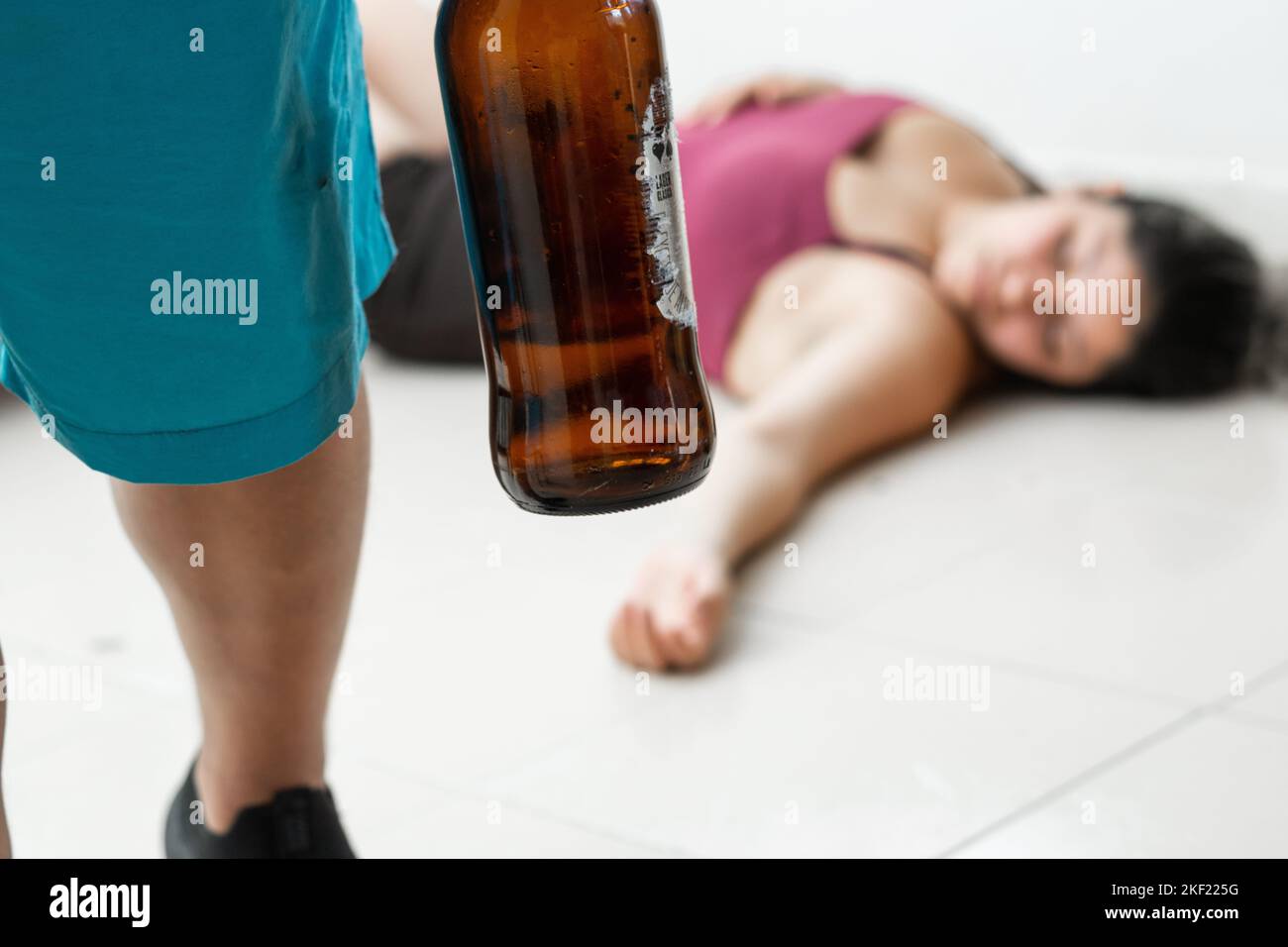 homme avec une bouteille de bière dans la main, laissant sa femme couché sur le sol après l'avoir battue. violence domestique et abus de femmes Banque D'Images