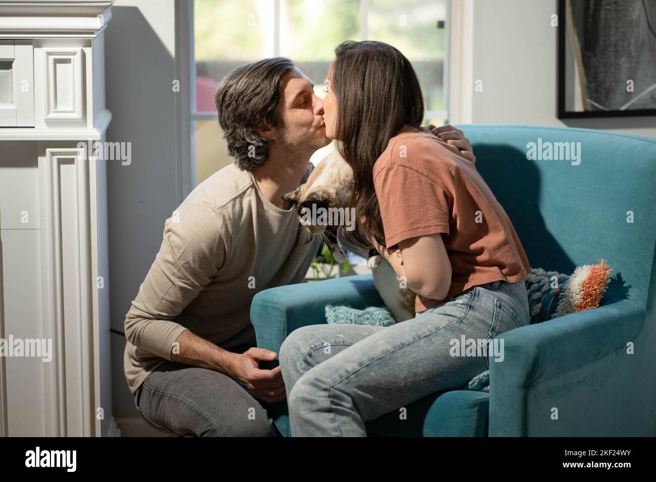 Un homme et une femme dans leur salon avec leur chat, se blottant avec amour dans une chaise bleue. Banque D'Images