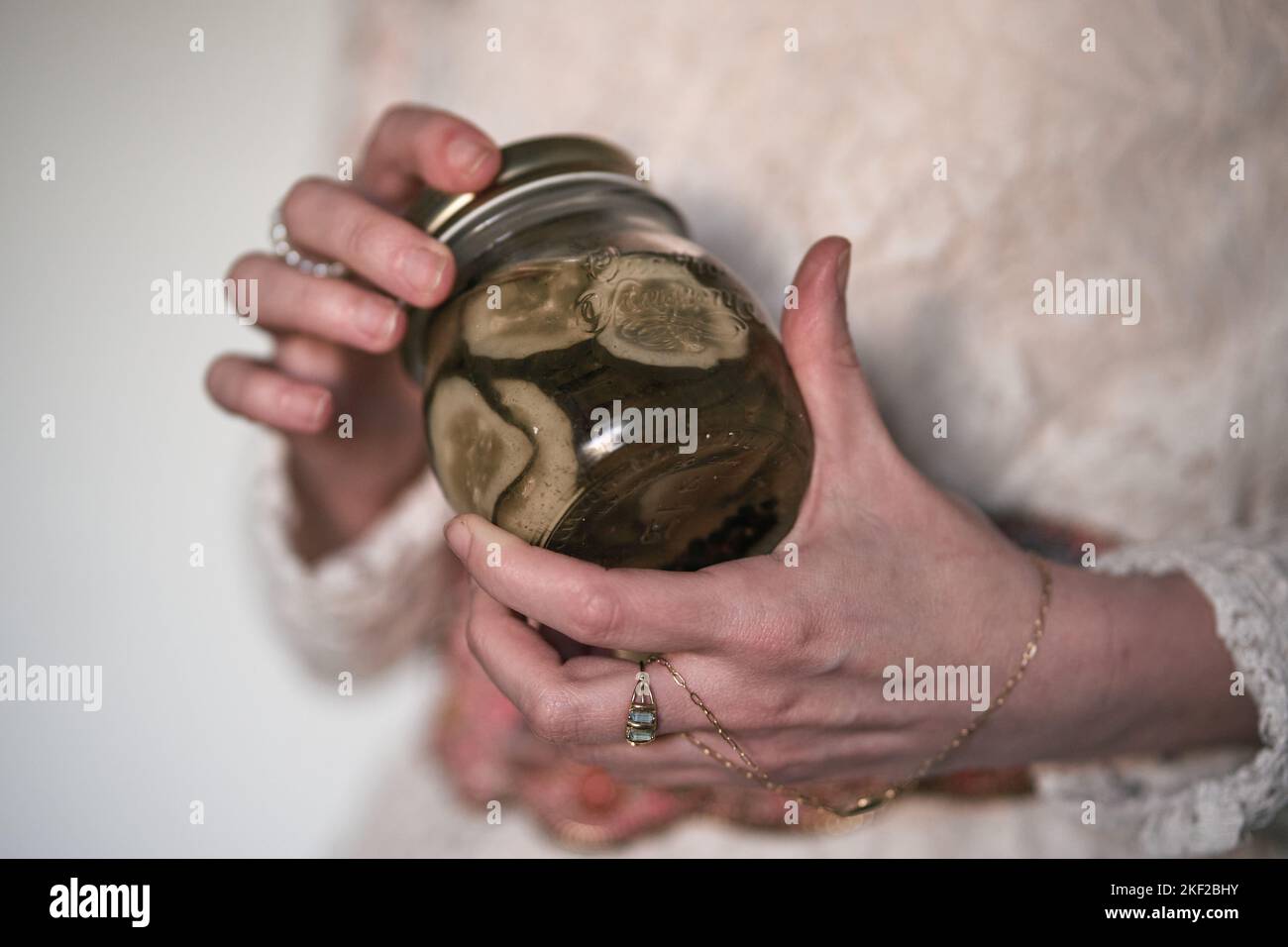 gros plan des mains d'une femme mature du caucase avec des anneaux et un bracelet tenant un pot en verre de concombre en conserve Banque D'Images