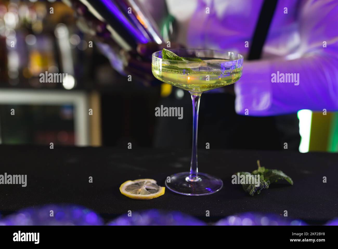 Milieu de section de barman afro-américain qui verse un cocktail vert au bar d'une discothèque Banque D'Images