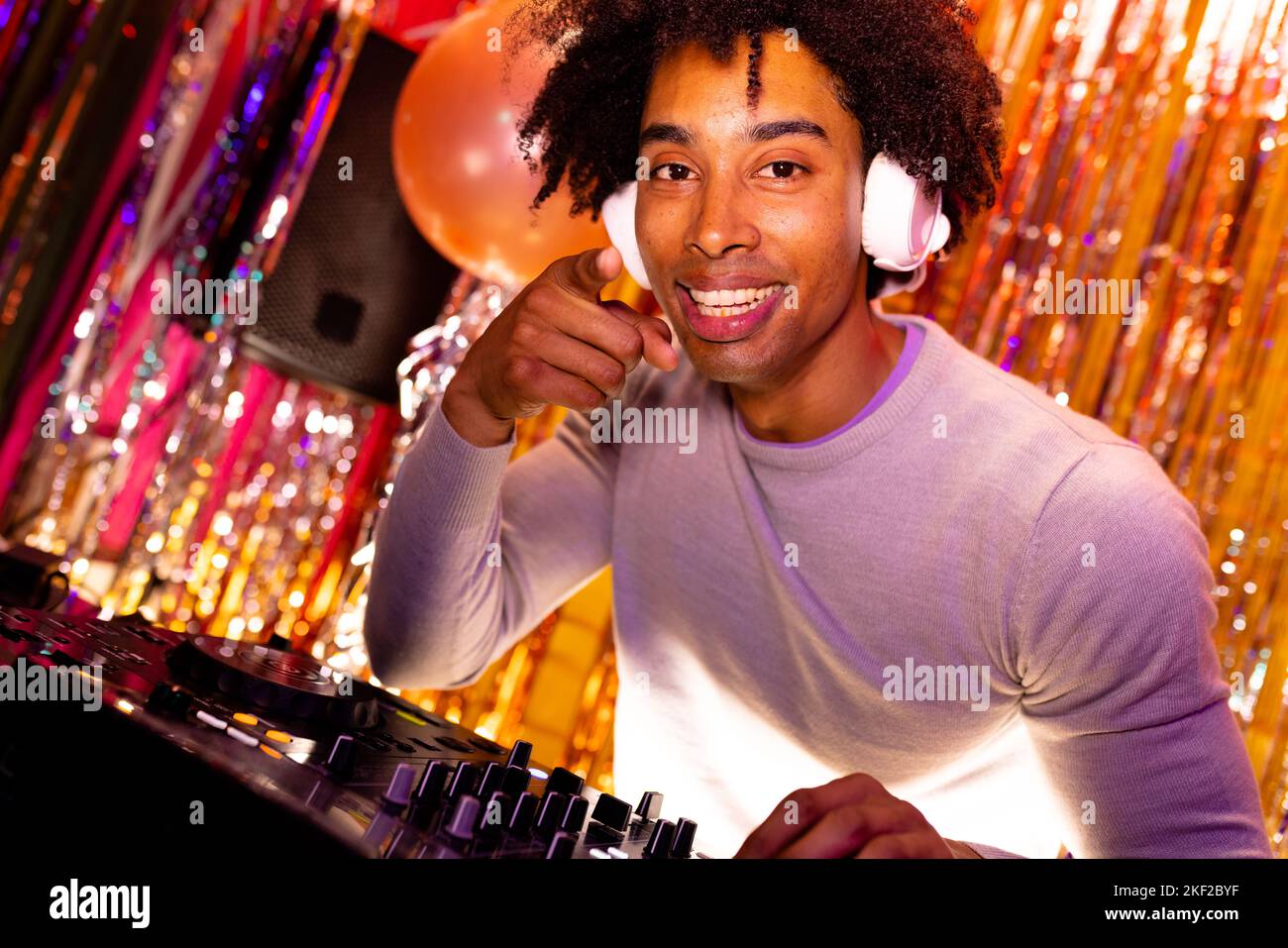 Portrait d'un DJ afro-américain souriant dans un casque jouant de la musique dans une boîte de nuit pointant Banque D'Images