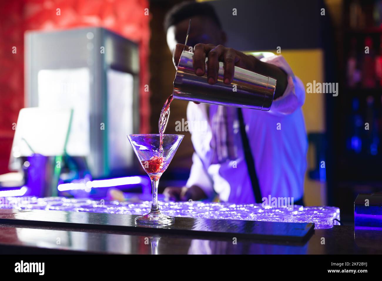 Le barman afro-américain verse un cocktail rose au bar d'une discothèque Banque D'Images