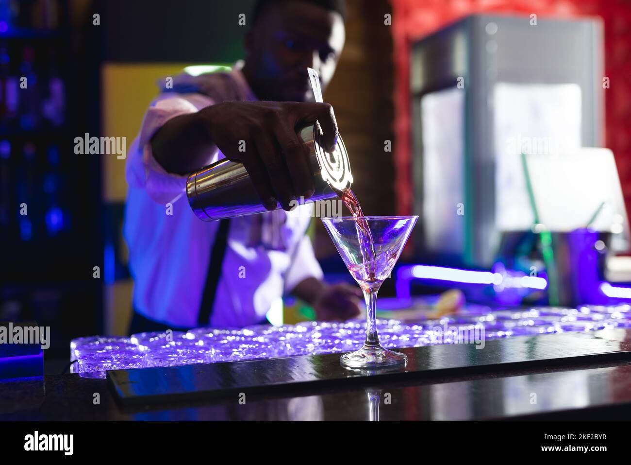 Le barman afro-américain verse un cocktail rose au bar d'une discothèque Banque D'Images