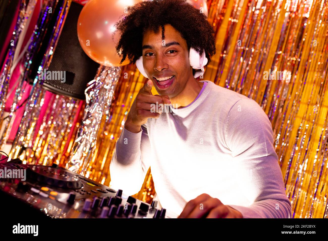 Portrait d'un DJ afro-américain souriant dans un casque jouant de la musique dans une boîte de nuit pointant Banque D'Images