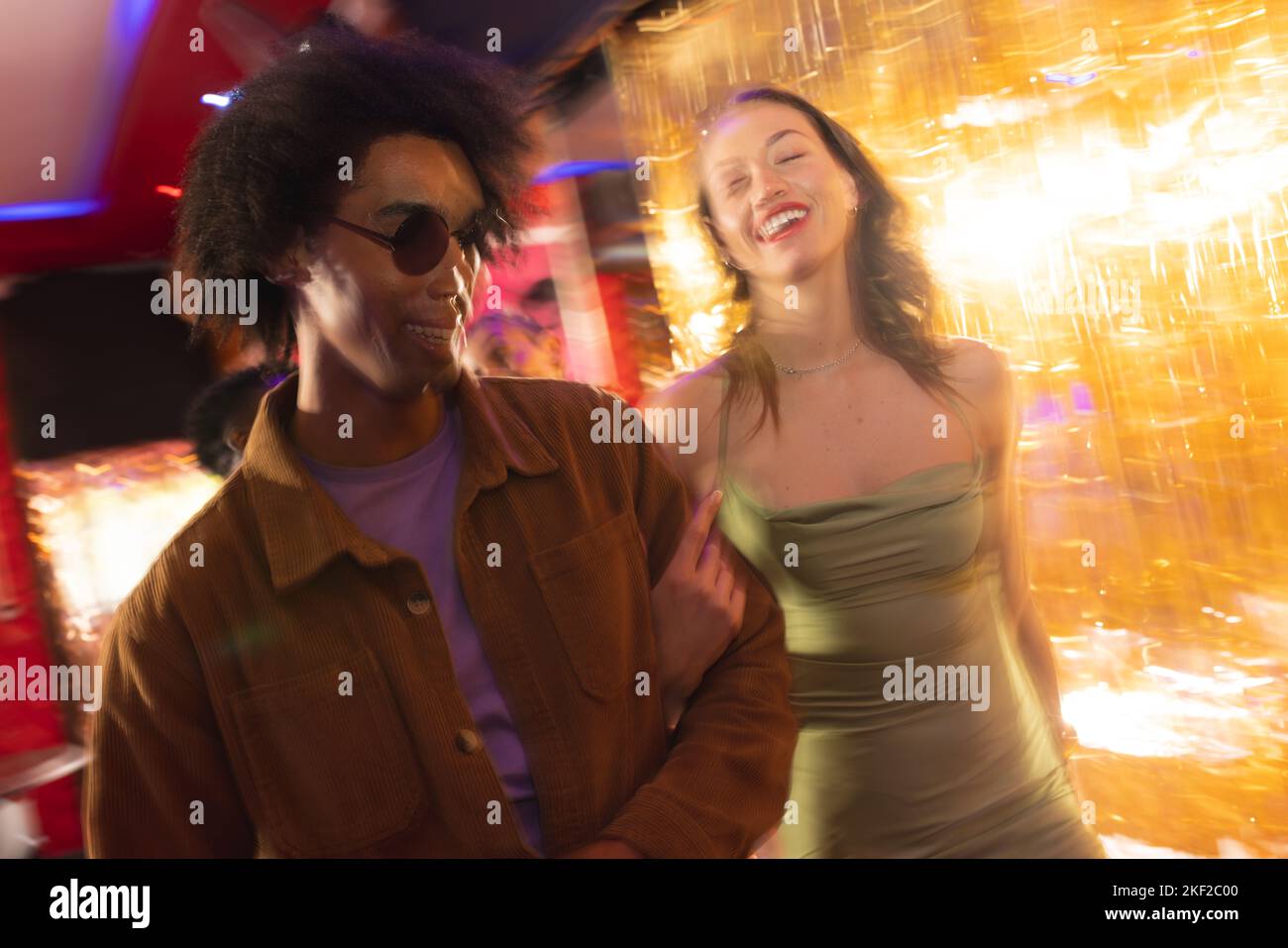 Un couple heureux et diversifié riant et marchant bras dans le bras dans une boîte de nuit Banque D'Images