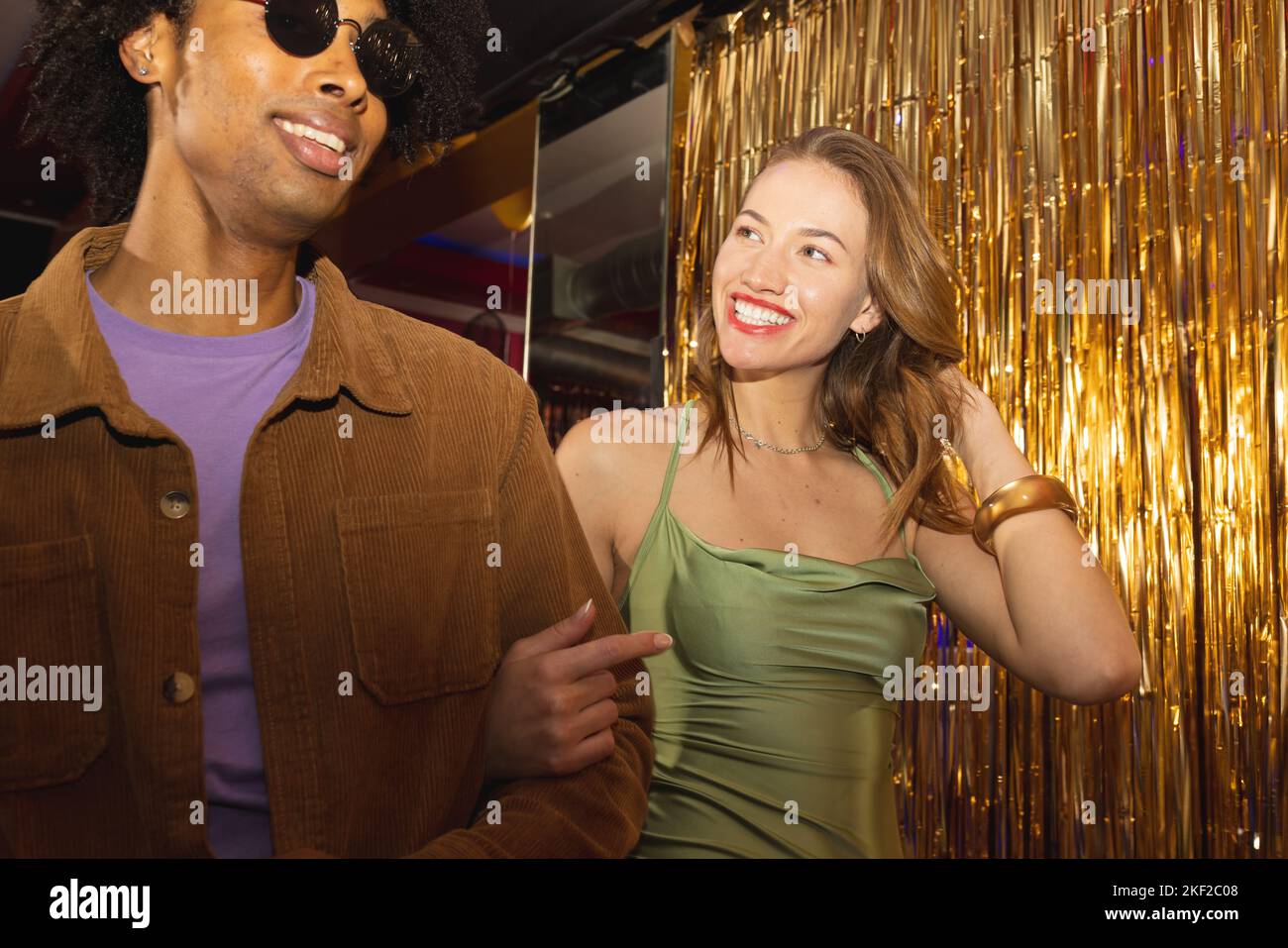 Un couple heureux et varié se souriant les uns aux autres et marchant bras dans le bras dans une boîte de nuit Banque D'Images