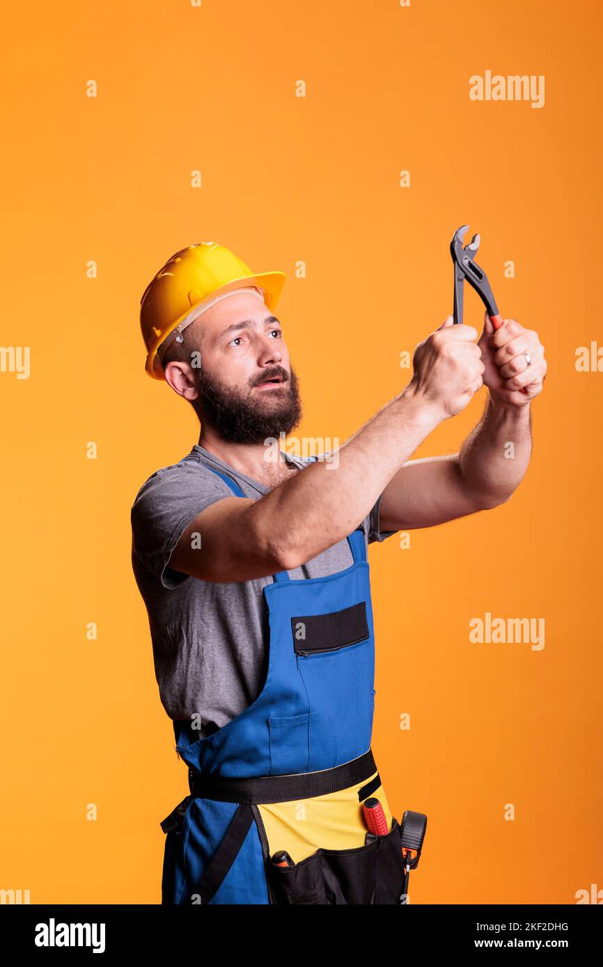Jeune contremaître constructeur regardant la paire de pinces, en utilisant des outils de construction sur fond jaune. Homme expert en rénovation ou menuisier travaillant avec des pinces pour le projet de rénovation. Banque D'Images