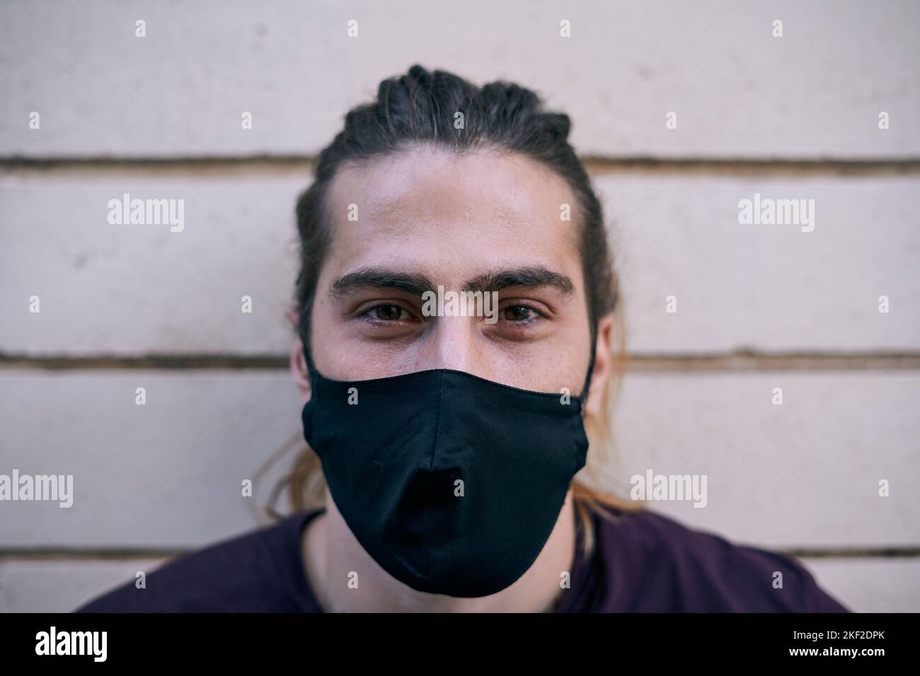 gros plan jeune homme caucasien avec des cheveux longs t-shirt noir et masque de visage regardant l'appareil photo Banque D'Images