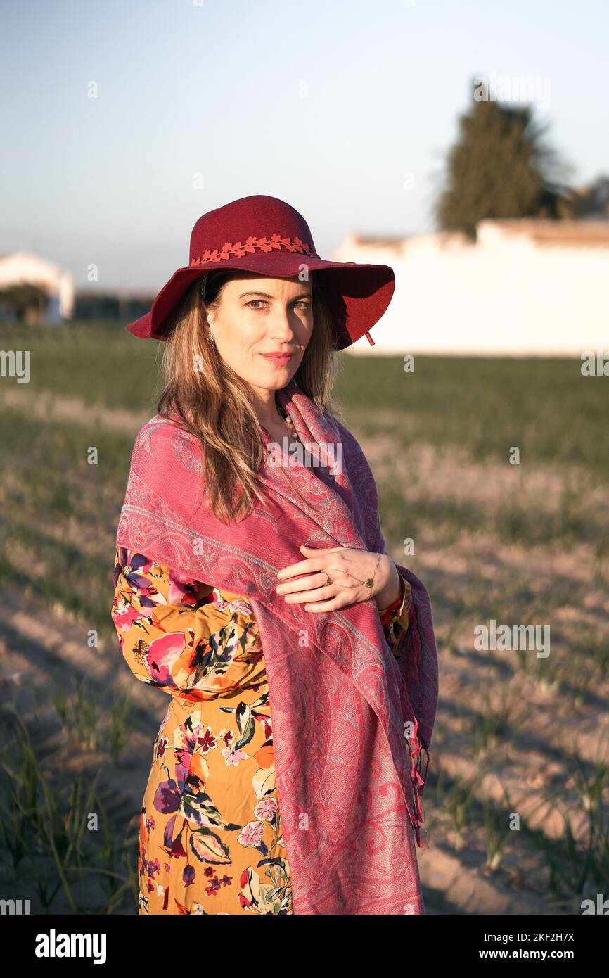 Caucasienne femme mûre debout dans une robe florale et châle rose regardant la caméra souriant du verger un jour ensoleillé Banque D'Images