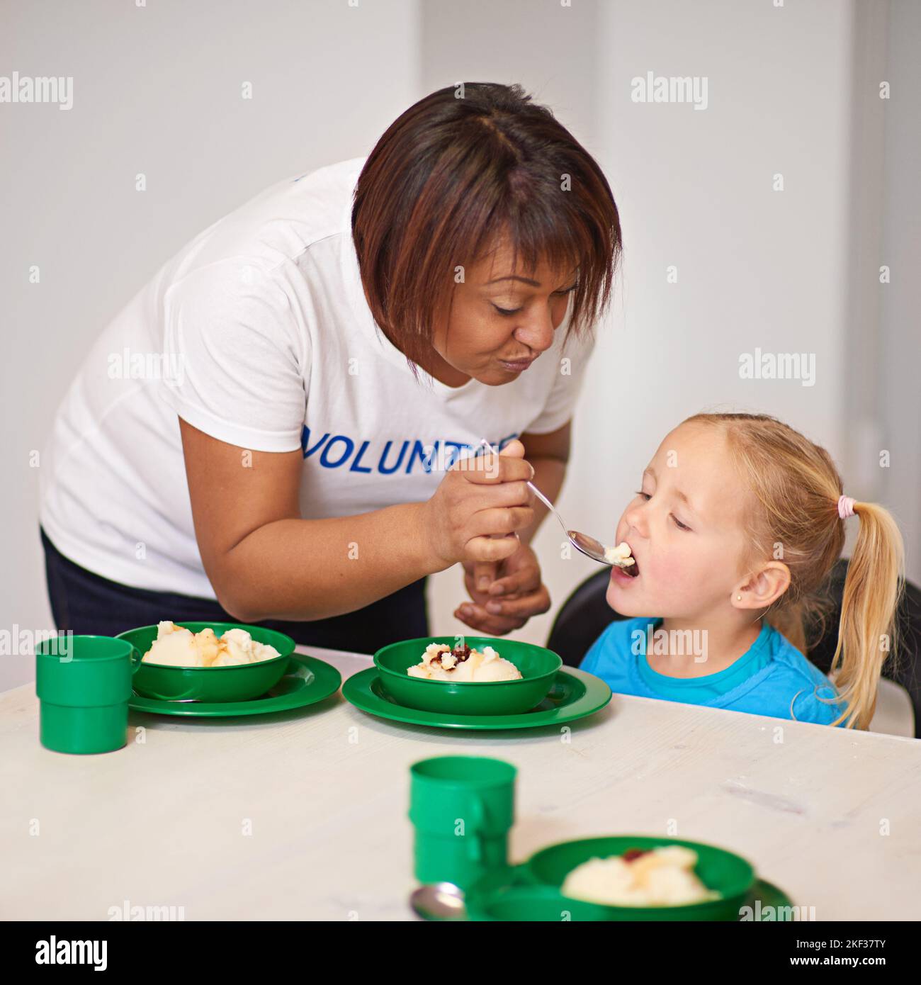 Fournir des repas nutritifs une cuillerée à la fois. Un volontaire nourrissant une petite fille dans un centre de jeunes. Banque D'Images