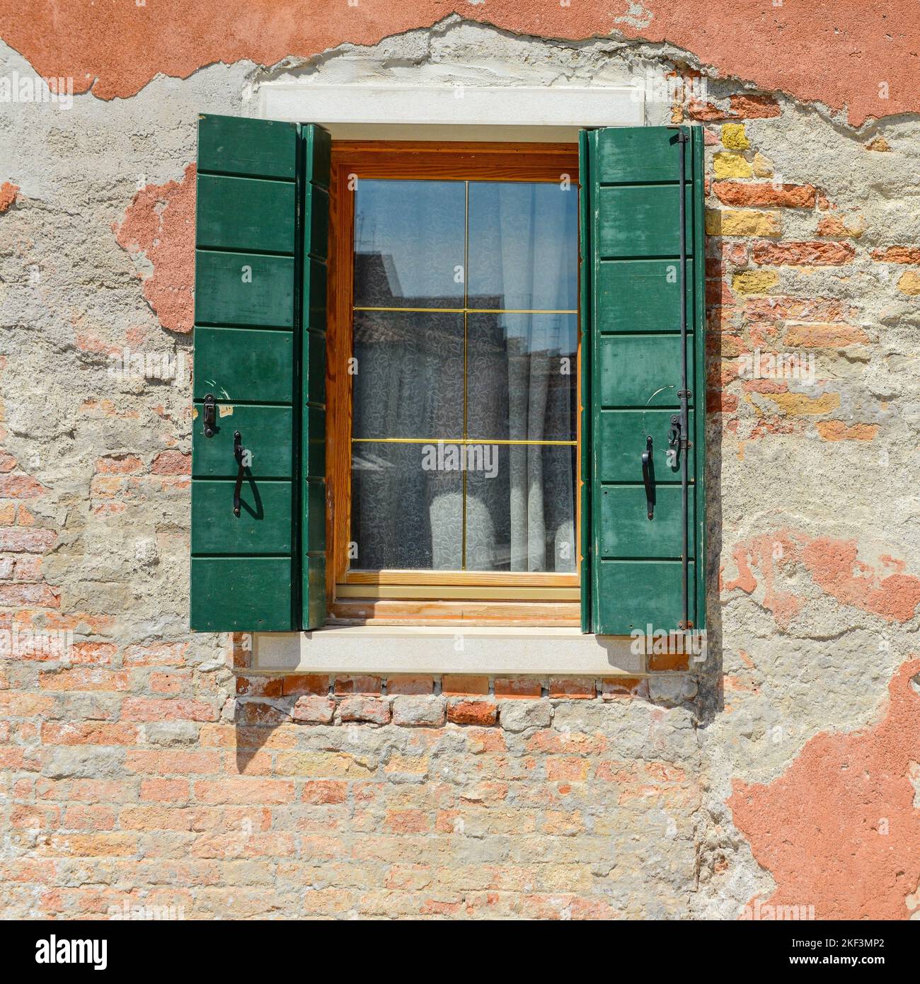 Fenêtre verte sur la vieille maison orange fissures dans le béton briques rouges visibles à Burano, Italie. Banque D'Images