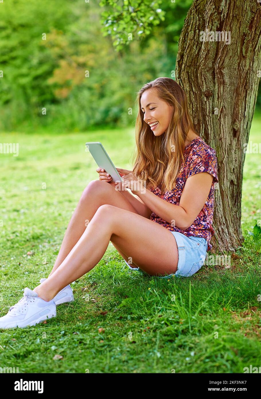 Elle passe son temps libre dans l'air frais. Une jeune femme utilisant une tablette numérique dans le parc. Banque D'Images