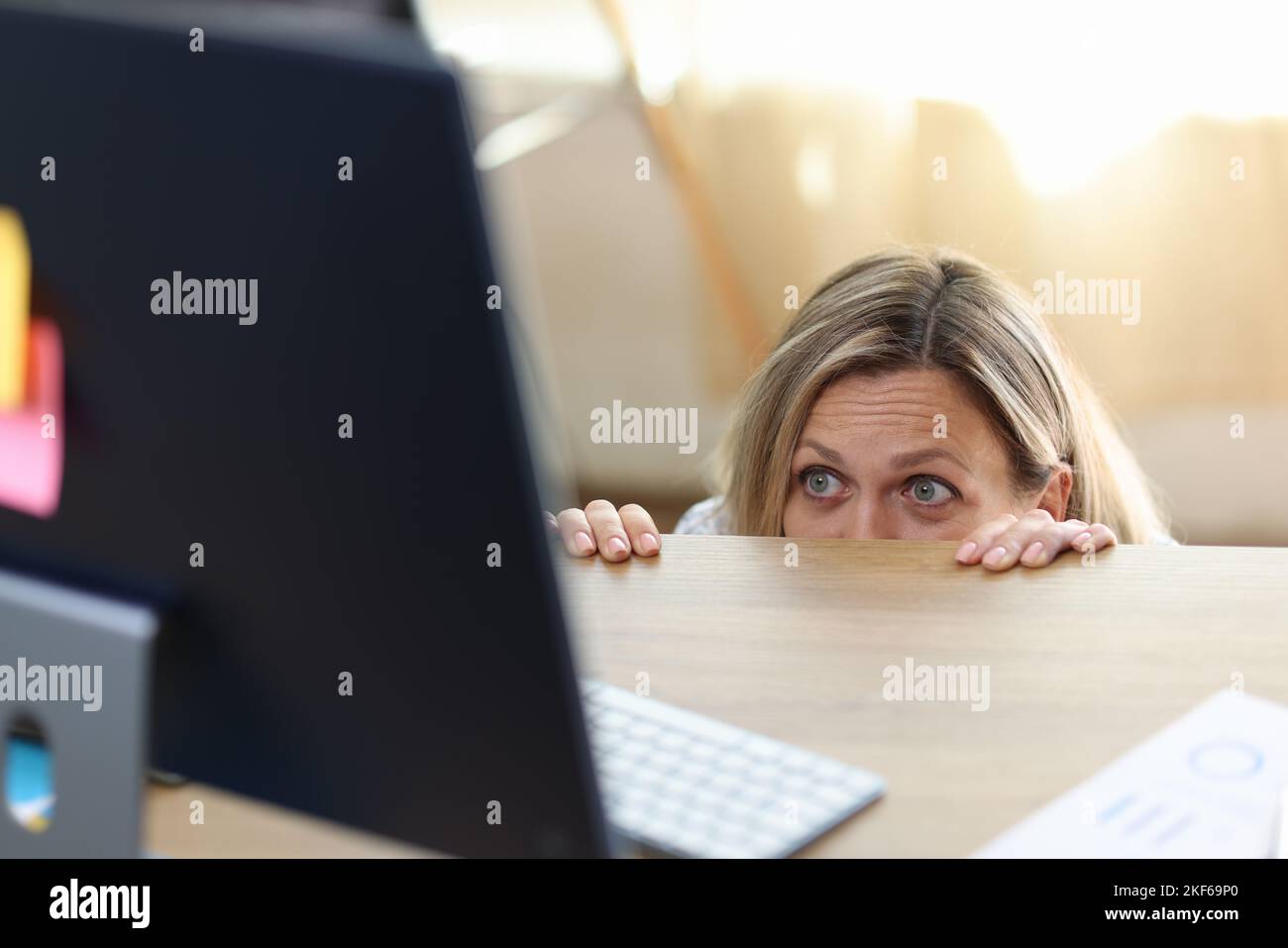 Femme effrayée et choquée dans la panique derrière le bureau regardant l'écran d'ordinateur. Banque D'Images