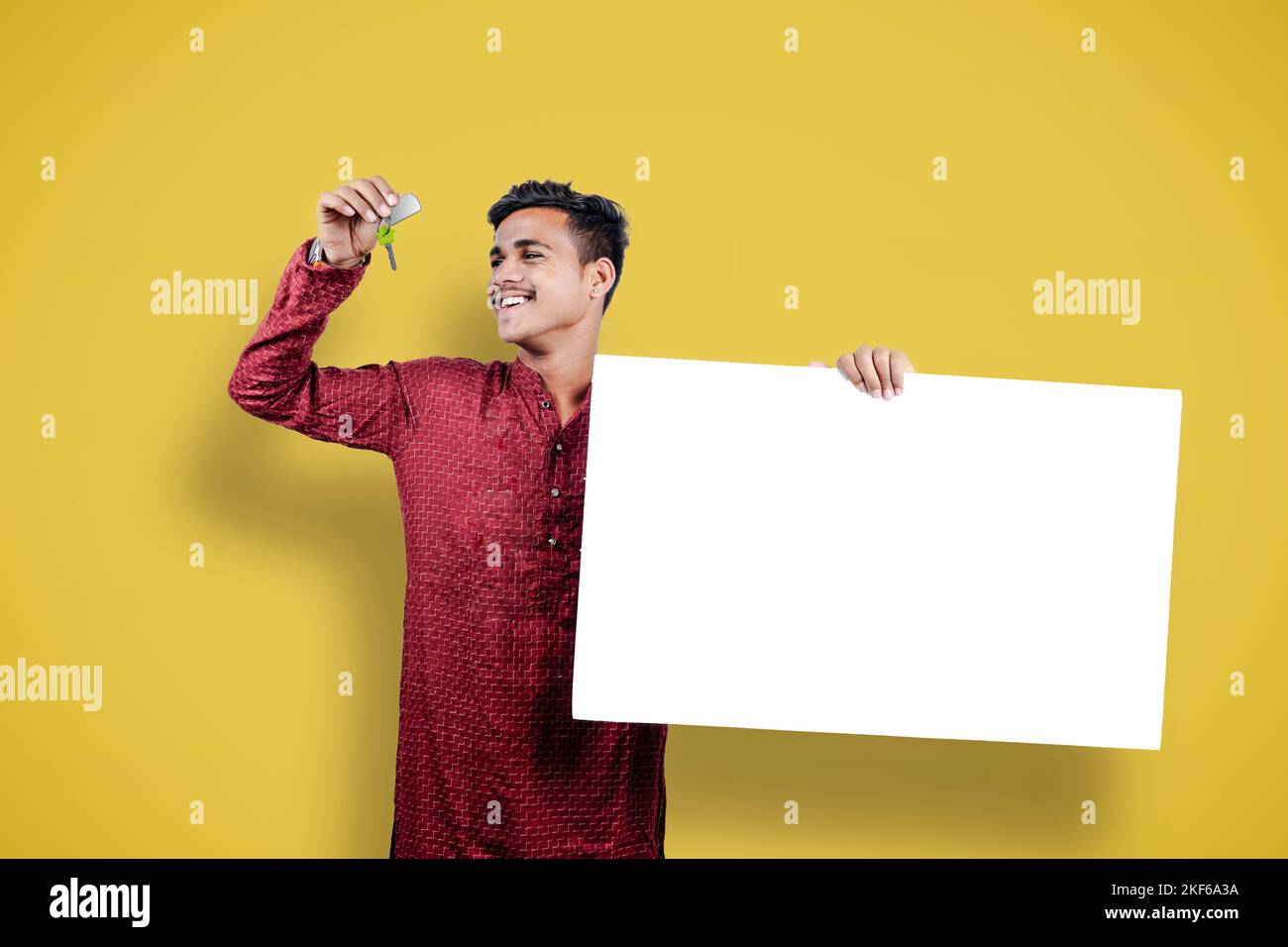 Homme montrant la clé de la maison sur le festival indien DIWALI et tenant le tableau blanc isolé sur fond jaune Banque D'Images