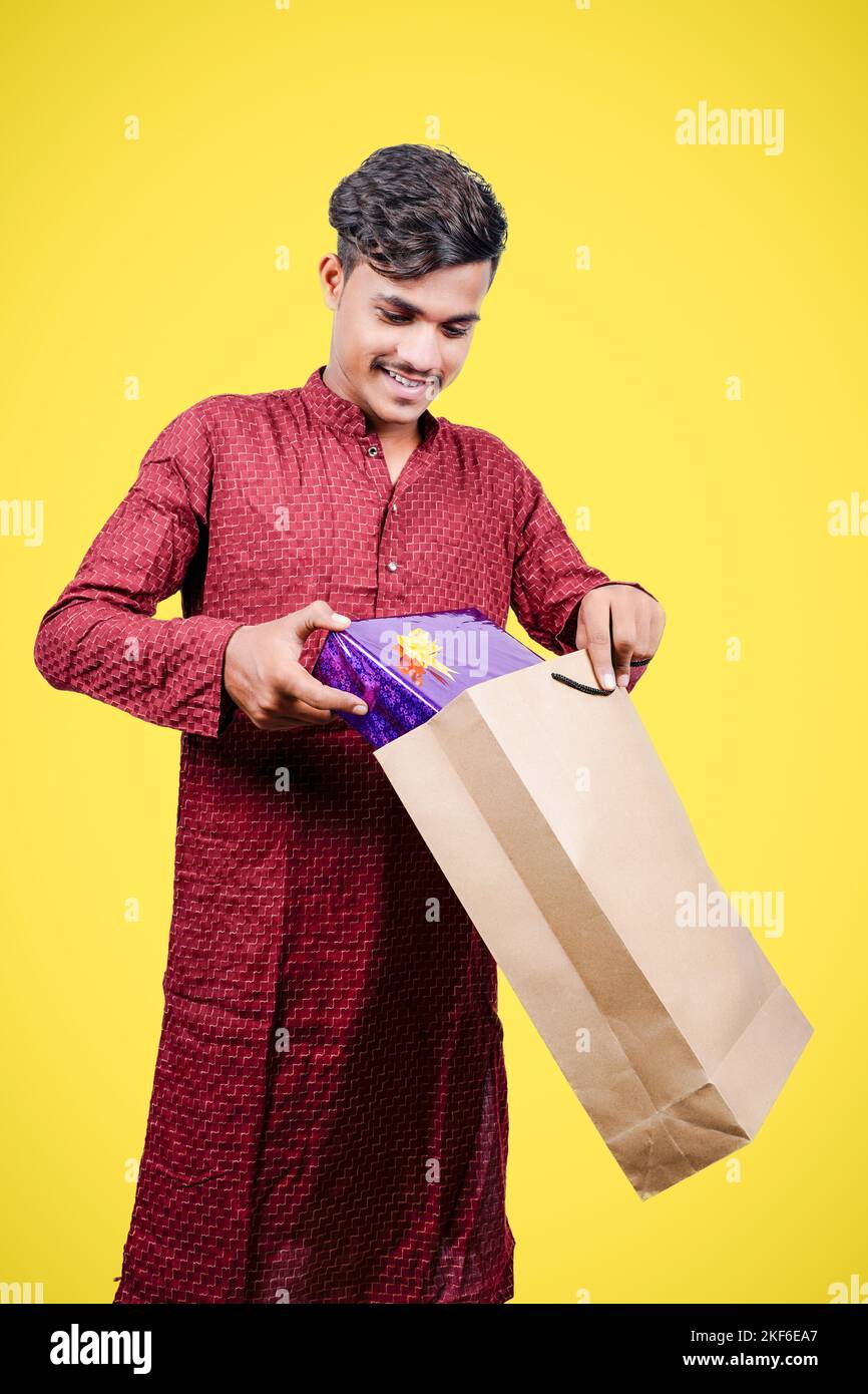 Homme indien en tenue ethnique avec garder ou laisser le cadeau dans des sacs de shopping, isolé sur fond jaune Banque D'Images