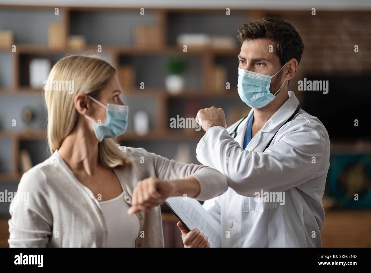 Un médecin portant un masque médical de protection se cognant les coudes avec une patiente Banque D'Images