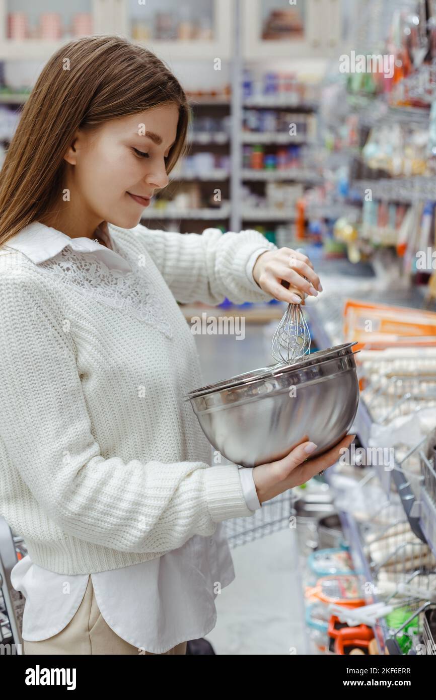 Une jeune femme choisit un bol en acier et fouette au rayon ustensiles de cuisine du supermarché. Banque D'Images