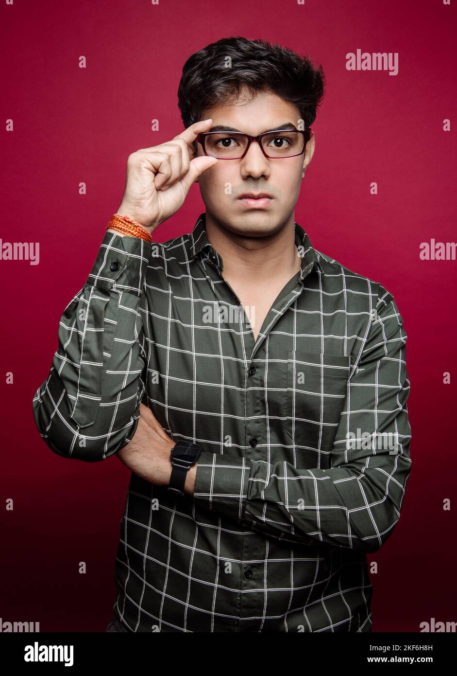 Portrait d'un homme d'Asie du Sud avec une expression sérieuse tout en tenant ses lunettes sur un fond rouge Banque D'Images