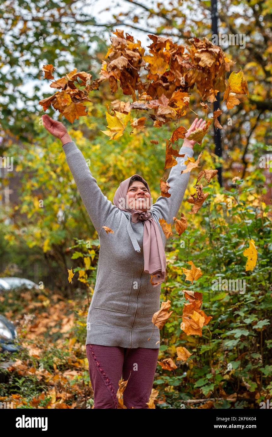 En automne, à Coventry, West Midlands, au Royaume-Uni, une femme jette des feuilles tombées dans l'air. Banque D'Images