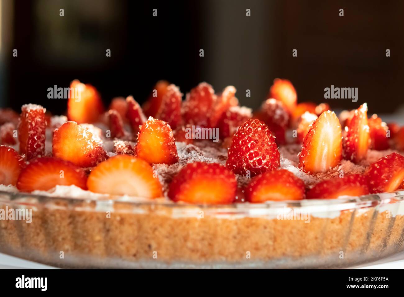 Tarte aux fraises noix de coco arrosée vue latérale macro photographie dans une plaque circulaire sous la lumière naturelle du jour. Faible profondeur de champ avec mise au point sélectionnée. Banque D'Images