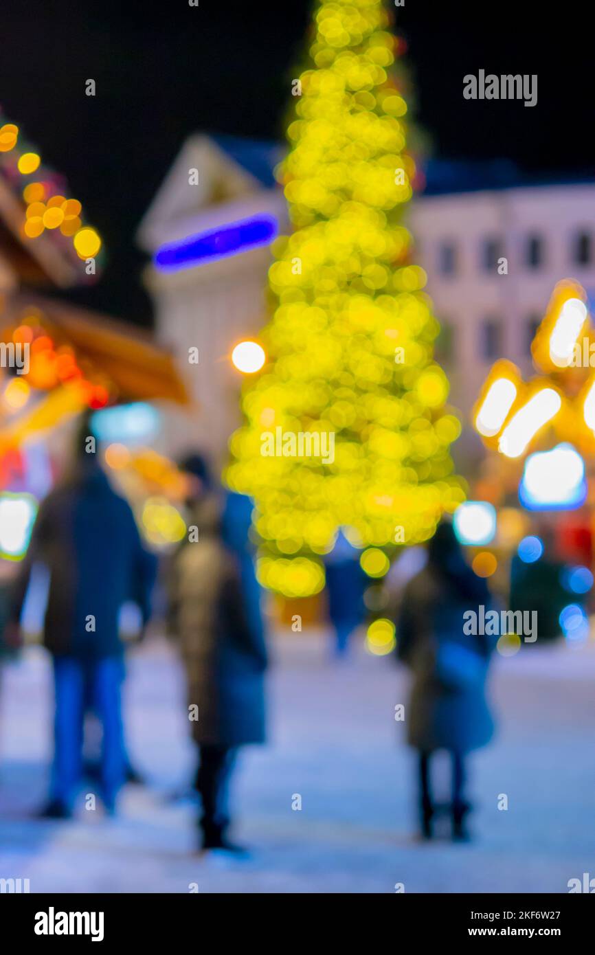 Arrière-plan flou. Noël nouvel an arbre décoré jaune guirlande illuminée, petites maisons en bois guirlande de lanternes sur le toit et silhouettes de personnes marchant le long de la rue de la ville. Vidéo verticale Banque D'Images