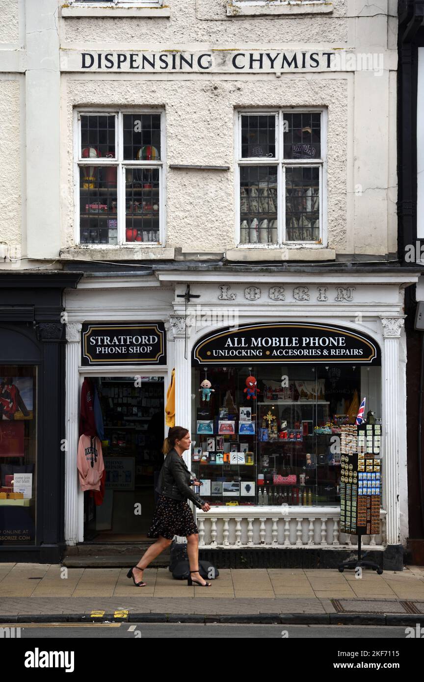 Une femme passe devant un ancien magasin de produits anciens ou anciens, un ancien chimiste distributrice maintenant un magasin de téléphonie mobile Stratford-upon-Avon Angleterre Banque D'Images