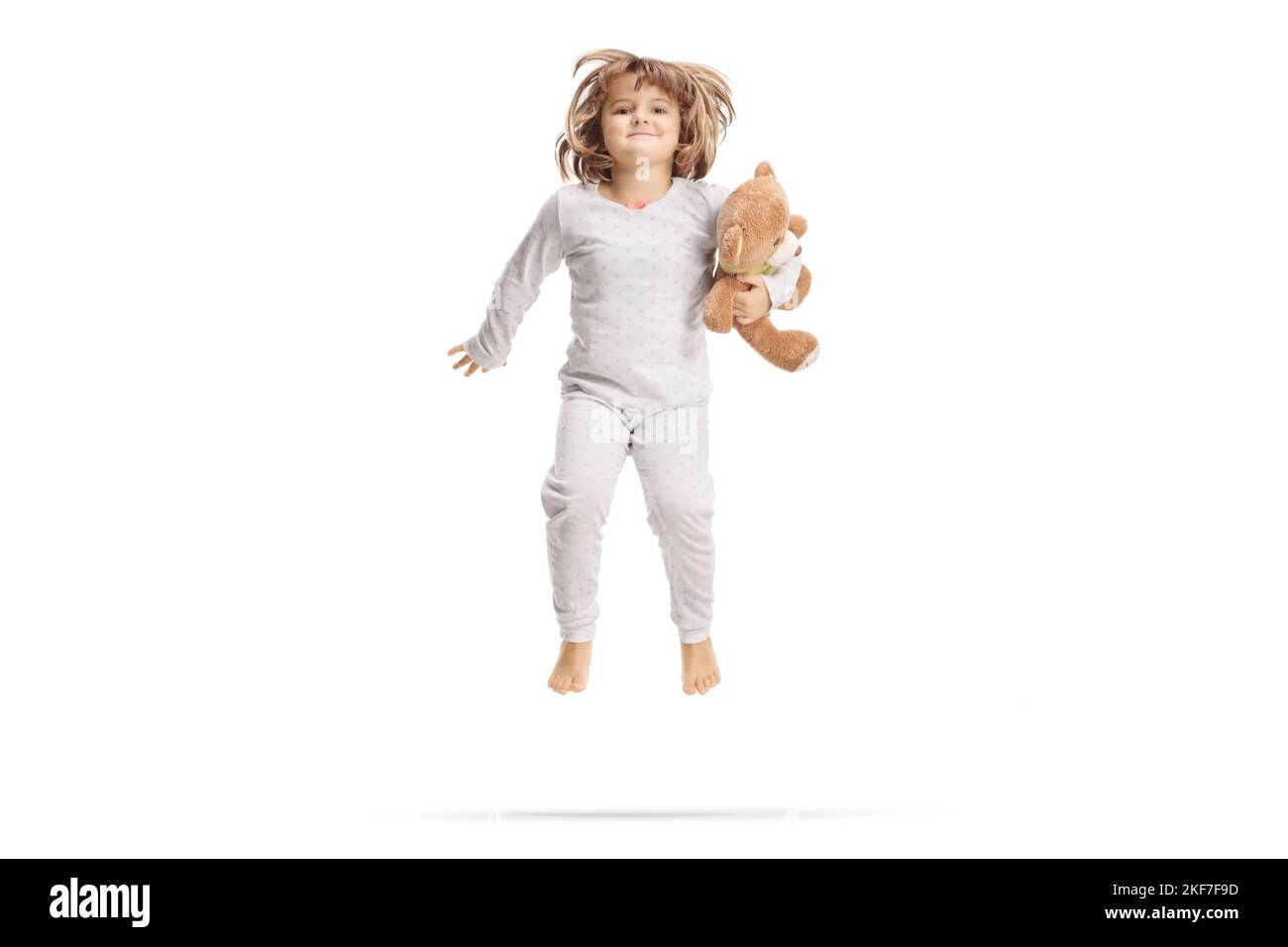 Petite fille en pyjama tenant un ours en peluche et sautant isolé sur fond blanc Banque D'Images
