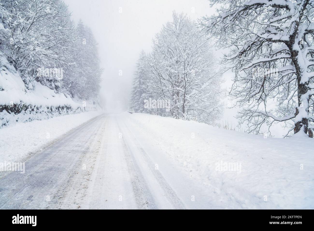 Mauvaise visibilité le long d'une route de montagne enneigée pendant une tempête de neige hivernale. Conditions de conduite dangereuses. Banque D'Images