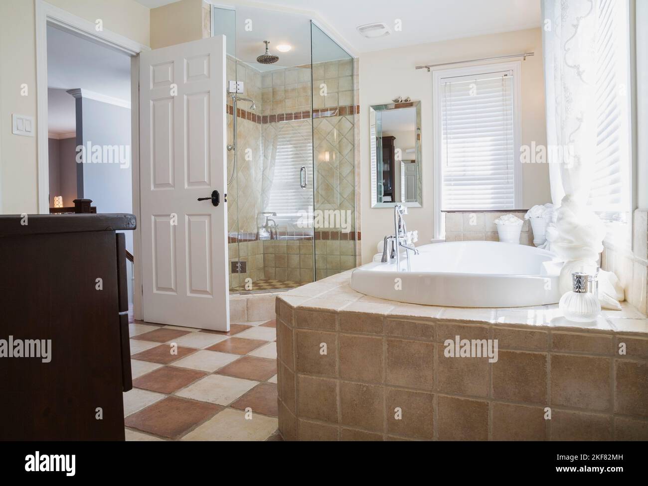 Baignoire profonde encastrée dans une base en céramique marron et beige et cabine de douche en verre dans la salle de bains principale à l'étage à l'intérieur de la maison contemporaine. Banque D'Images