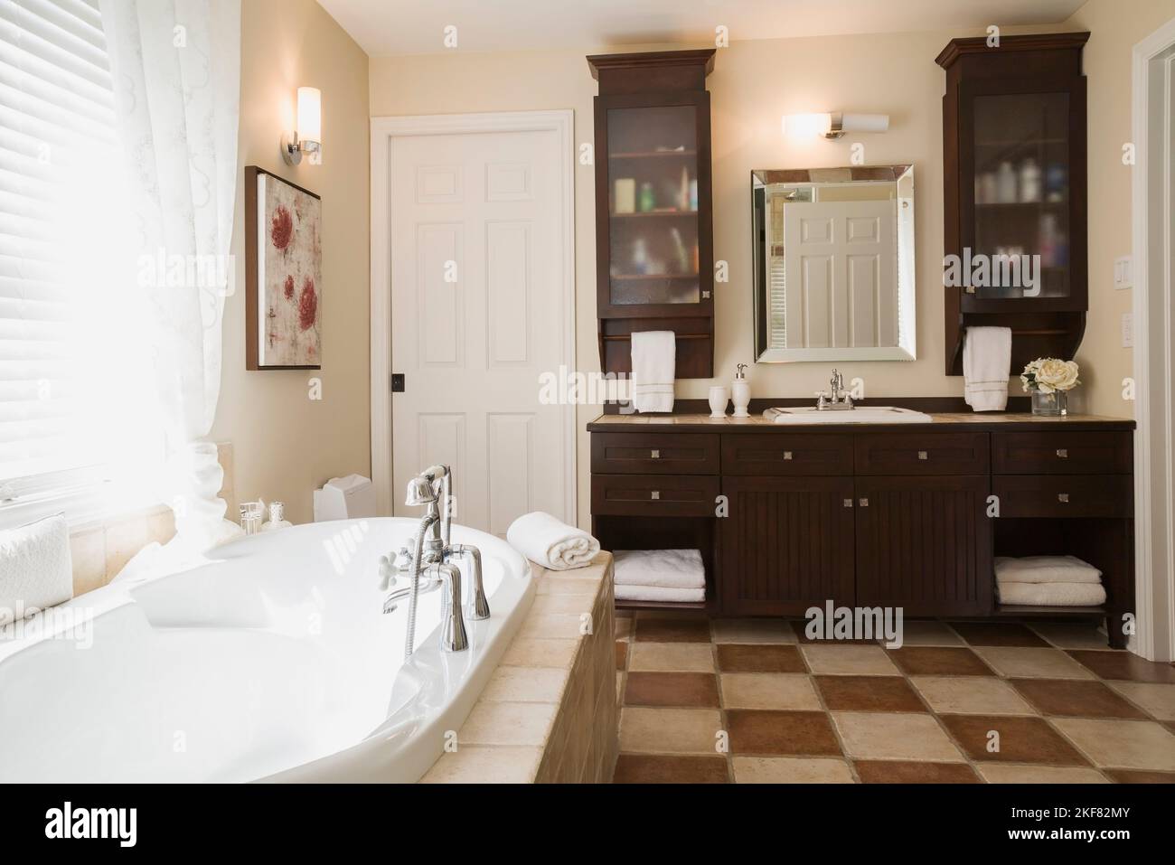 Baignoire profonde encastrée dans une base en céramique marron et beige et vanité en bois dans la salle de bains principale à l'étage à l'intérieur de la maison contemporaine. Banque D'Images