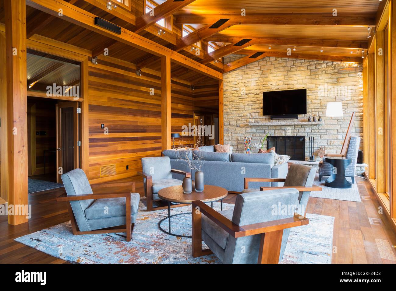 Fauteuils rembourrés en bois brun et gris, table ronde et canapés avec cheminée en pierre naturelle dans la salle de séjour à l'intérieur d'une maison en bois de cèdre. Banque D'Images